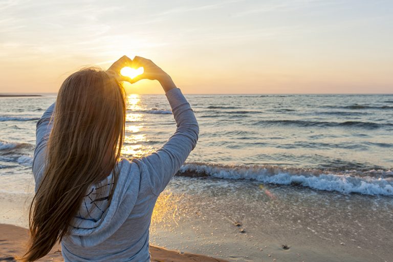 woman on the beach with heart hand sign
